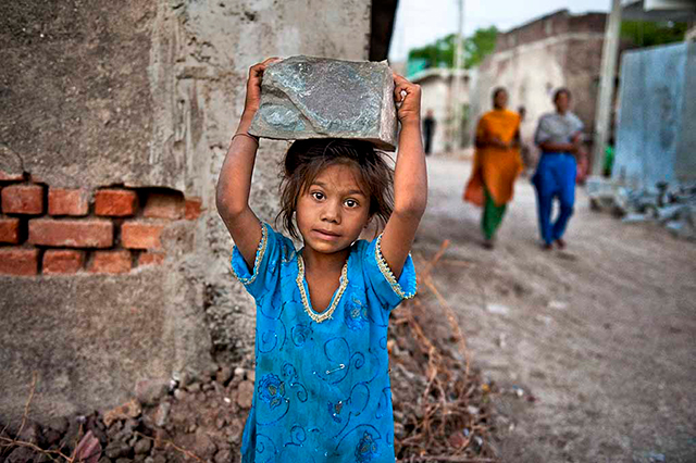 Steve McCurry Firenze foto a colori di piccola bambina vestita di azzurro che tiene un grosso sasso sulla testa