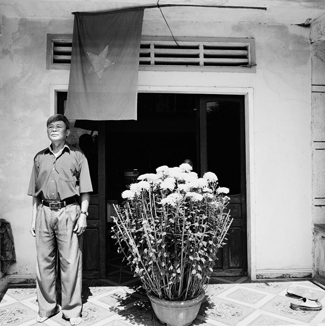 Nicola Bertasi Milano Foto in bianco e nero di uomo vietnamita in piedi vicino a grande vaso di fiori