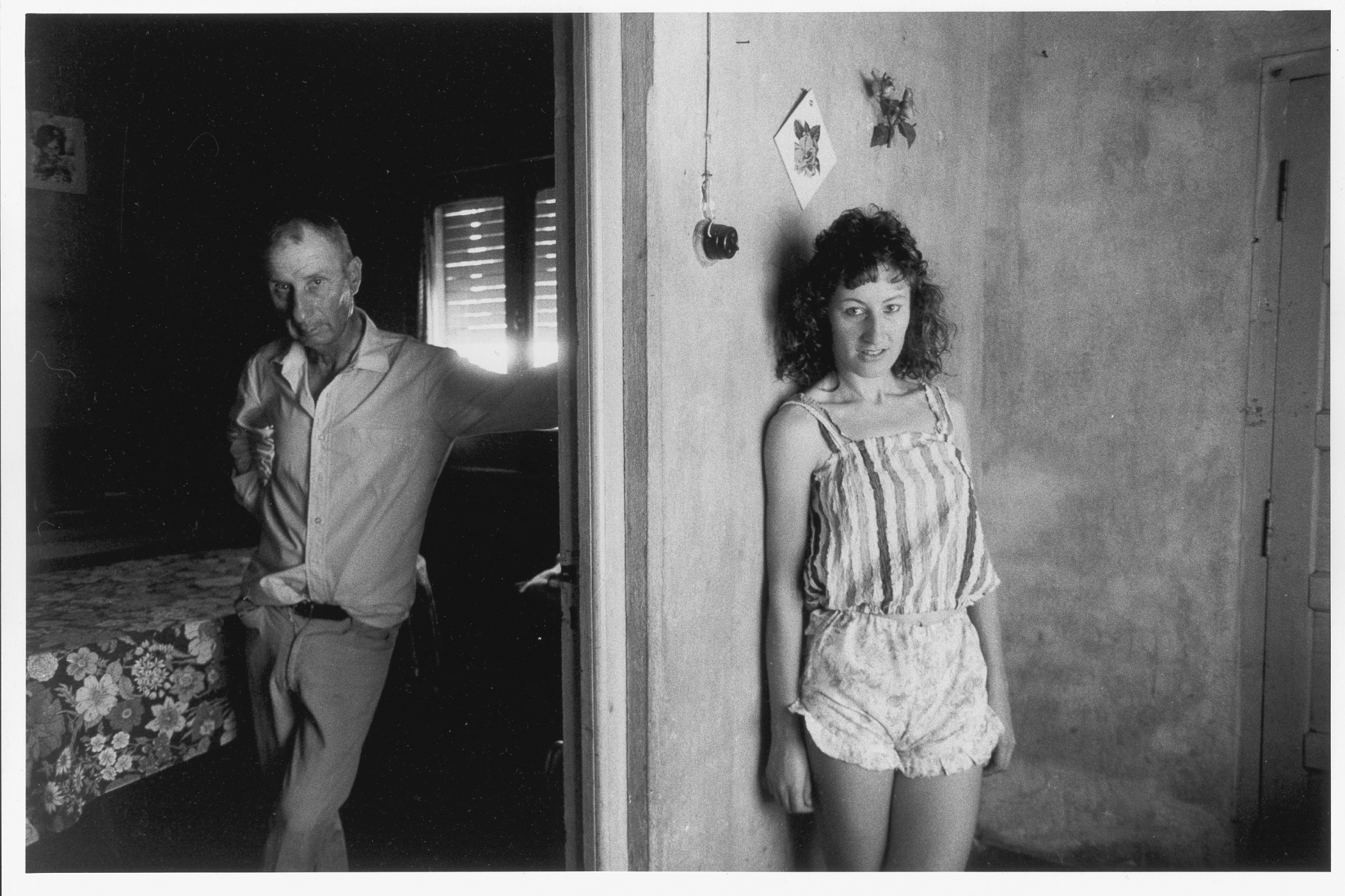 Paola Agosti Palau foto in bianco e nero di donna appoggiata al muro di una casa con uomo che esce da una stanza