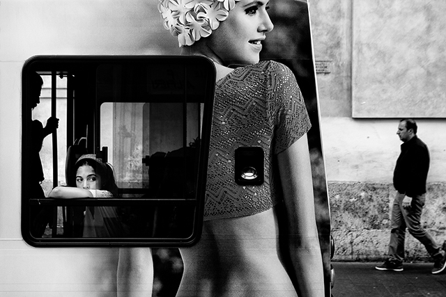 Stefano Mirabella Roma foto in bianco e nero di bambina che guarda fuori dal finestrino di un autobus con pubblicità di modella sulla fiancata