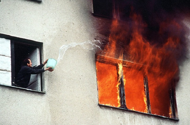 Sanremo Humanrights Photo Festival foto a colori di uomo che da finestra di un palazzo tenta di spegnere incendio nella finestra accanto