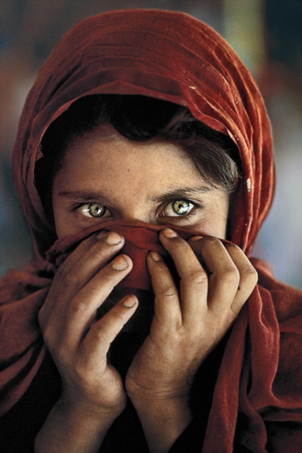 Steve McCurry Genova primo piano a colori di bambina afghana con velo rosso in testa e mani sul viso