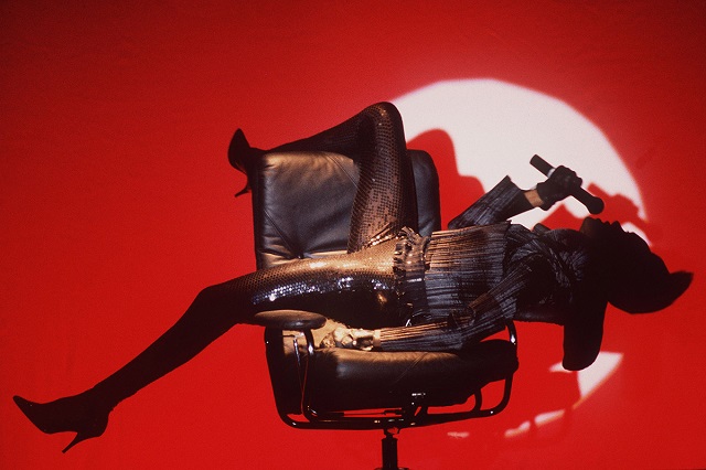 Mark Allan Fiorano Modenese foto a colori della cantante Grace Jones sdraiata su una sedia con microfono e sfondo rosso