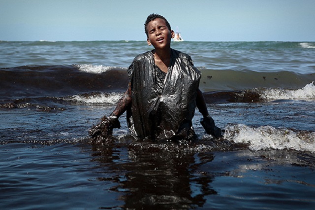 Non c'è più tempo Bard foto a colori di bambino che esce dal mare coperto di petrolio